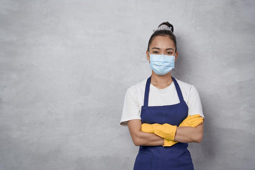 Confident cleaning lady wearing rubber gloves and medical protective face mask keeping arms crossed